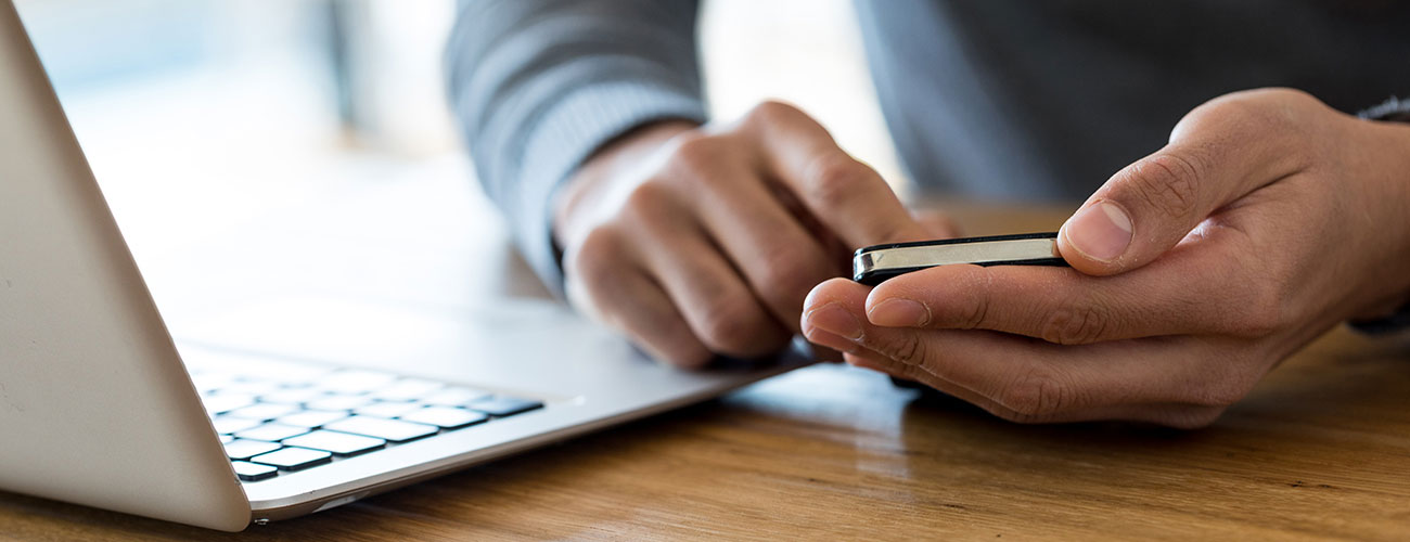 A person using their phone by a computer