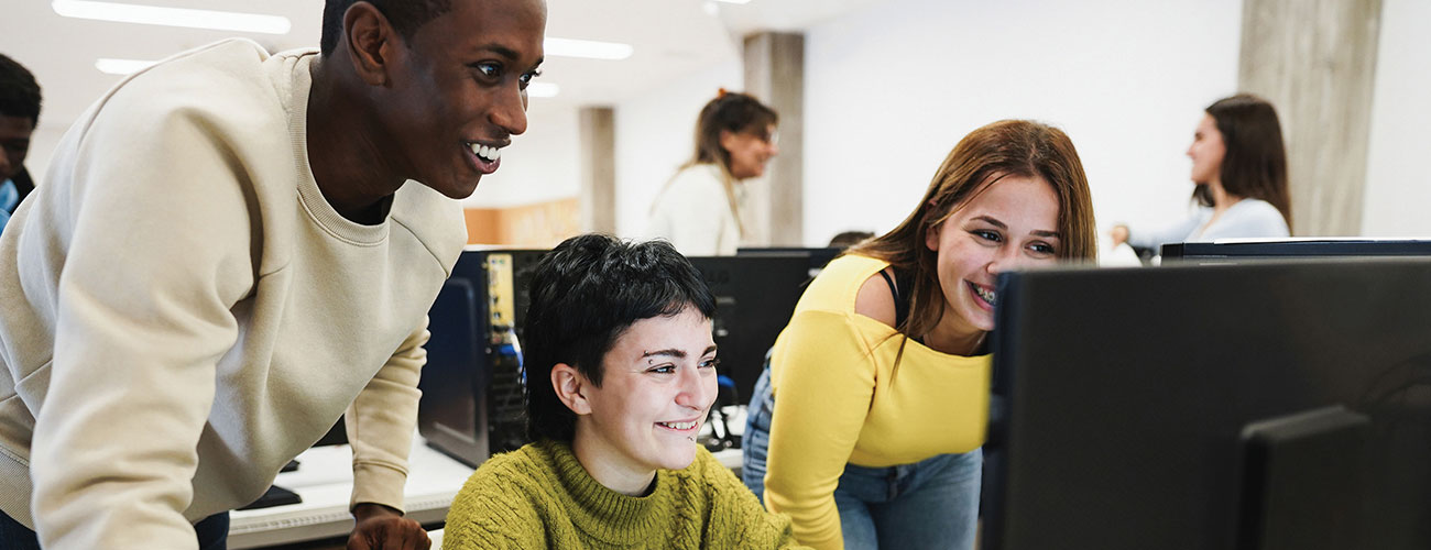 Three students gathered around a computer reviewing a digital media and technology project