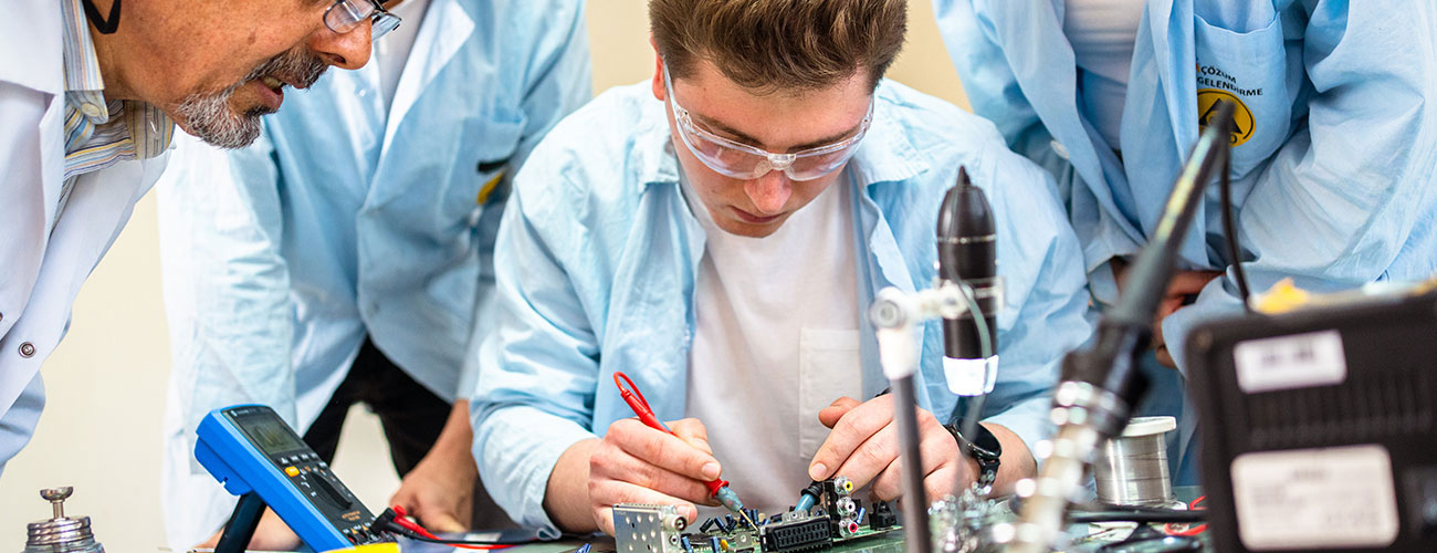 A male student surrounded by group while he's working on a project