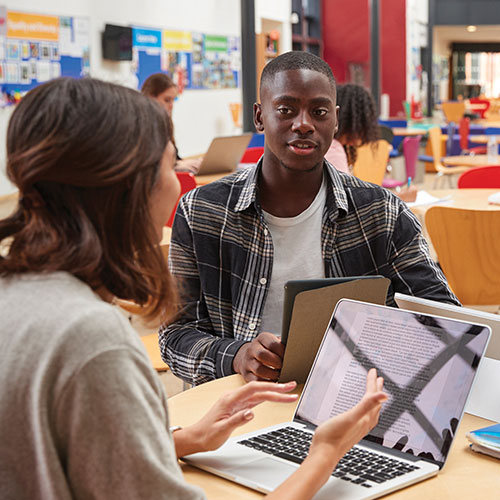 Two students sitting at a table in a classroom talking