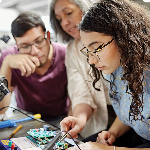 A partner helping two students with a real world hands on project