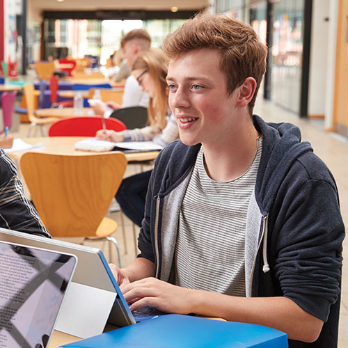 A male student sitting at a desk while working on a laptop
