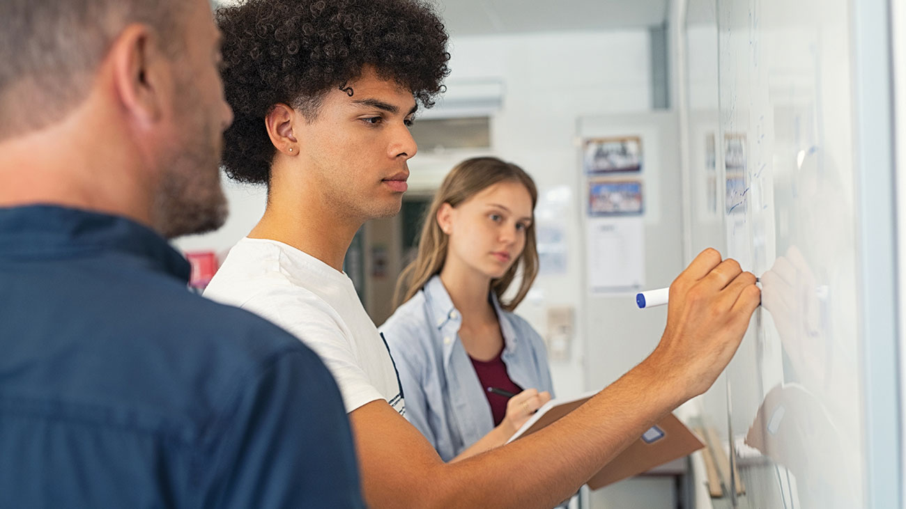 Two students at a board working out a problem with a business and entrepreneurship partner