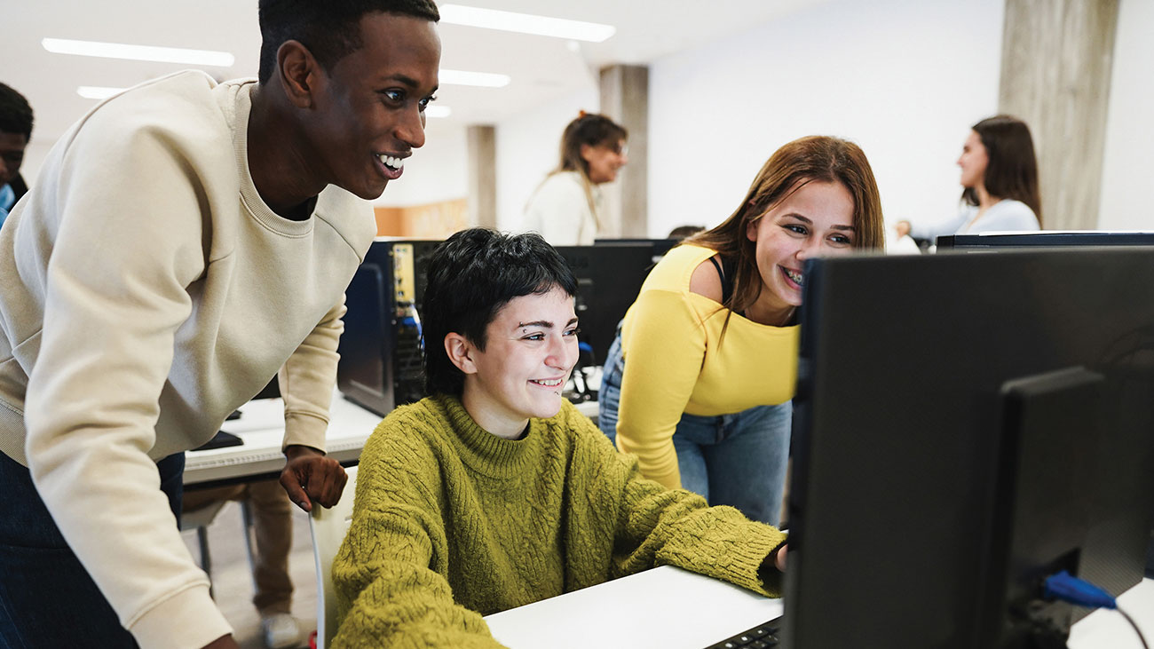 Three students gathered around a computer reviewing a digital media and technology project